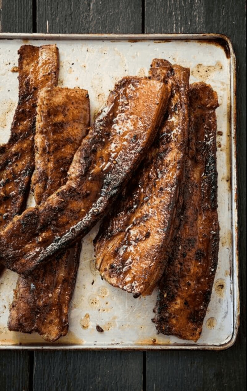 Grilled, browned slices of seasoned BBQ belly pork placed on a silver tray, reminiscent of a British classic from the Hairy Bikers