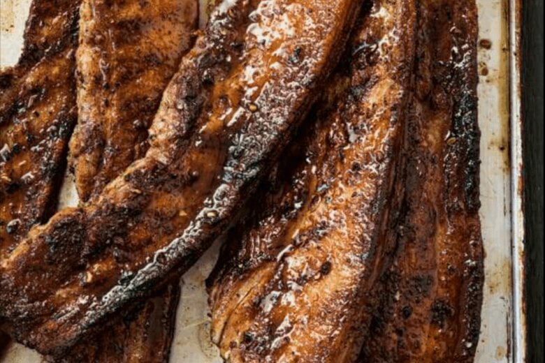 Grilled, browned slices of seasoned BBQ belly pork placed on a silver tray, reminiscent of a British classic from the Hairy Bikers