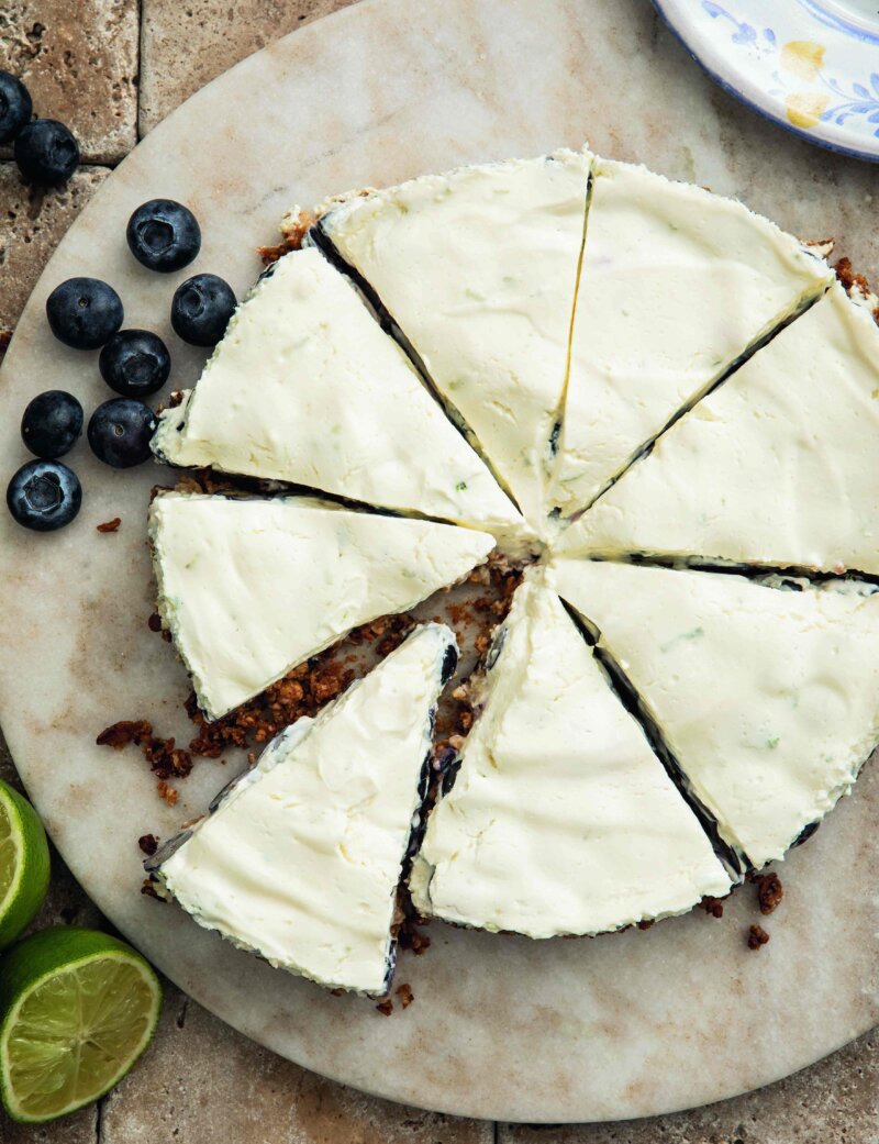 A blueberry cheesecake cut into slices on a marble plate, garnished with blueberries and lime slices.