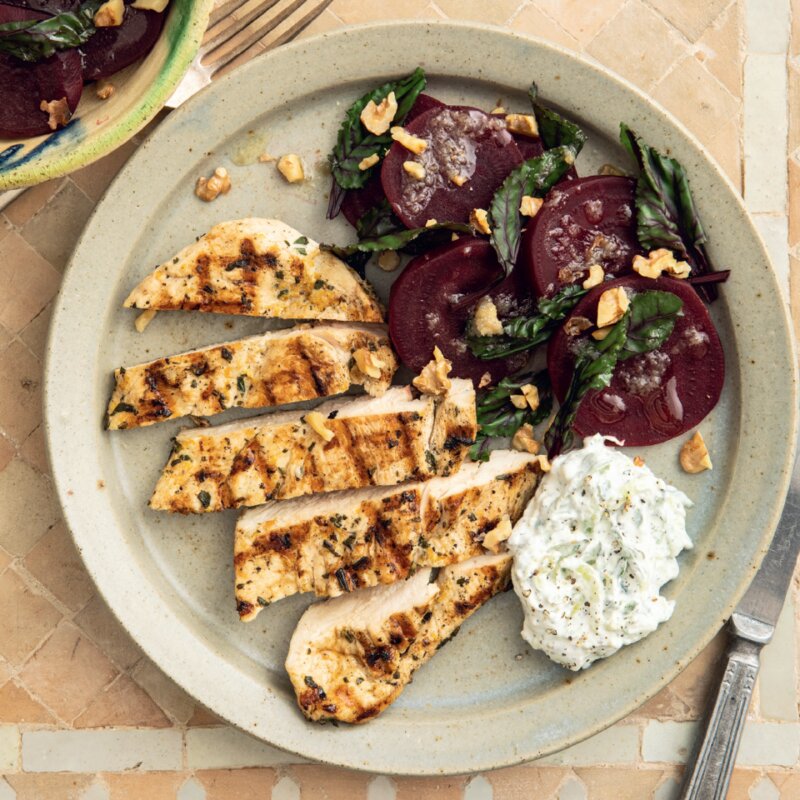 A plate with the Hairy Dieters' grilled chicken breast slices, a side of beet salad with chopped herbs, and a serving of tzatziki sauce.