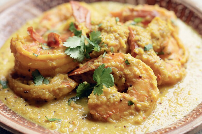 A plate of shrimp in a yellow curry sauce, inspired by a Keralan King Prawn Curry, garnished with fresh coriander