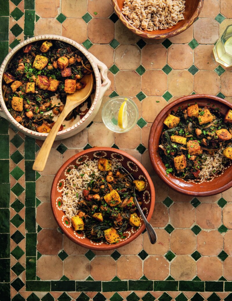 Traditional dishes with halloumi, spinach, and brown rice served in clay pots and bowls on a tiled table, accompanied by slices of lemon.