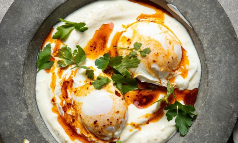 A plate of Turkish eggs with two poached eggs on a bed of yogurt, drizzled with chili-infused oil and garnished with fresh parsley, straight from the Hairy Dieters' Simple Healthy Food collection.